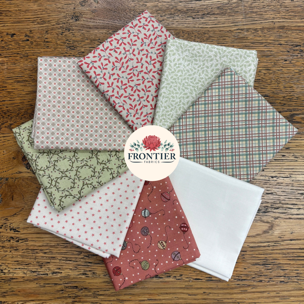 A set of Frontier Fabrics cotton fat quarters arranged in a fan shape on a rustic wooden background. The fabrics feature various patterns including plaid, polka dots, florals, and abstract prints in muted tones of red, green, pink, and white.