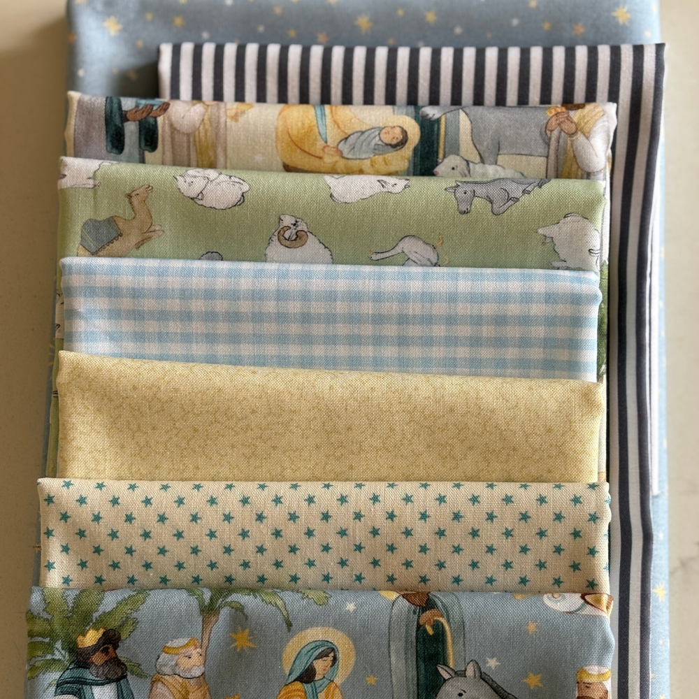 A stack of folded fabrics with various patterns including stripes, gingham, stars, and nativity scenes in soft pastel colours.