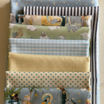 A stack of folded fabrics with various patterns including stripes, gingham, stars, and nativity scenes in soft pastel colours.