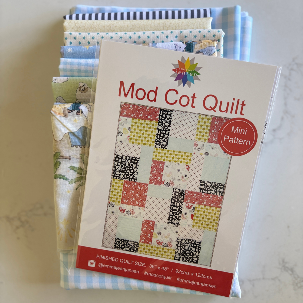 A selection of fabrics neatly placed on a blue gingham fabric with a pattern for Mod Cot Quilt on top