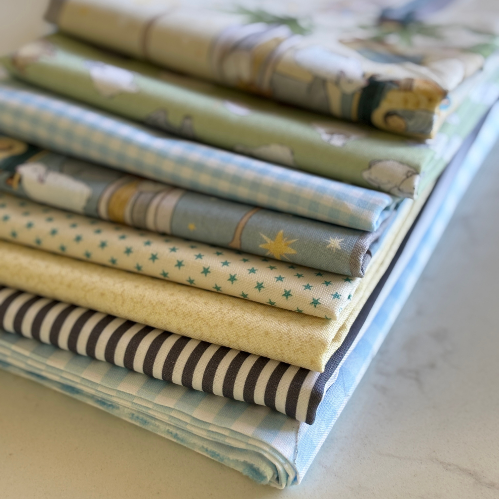 A stack of folded fabric pieces in soft pastel colors and patterns, including stripes, stars, gingham, and floral motifs, arranged on a light surface.
