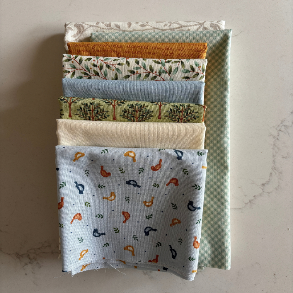 A stack of folded fabric pieces with various patterns and colours, including floral, checkered, and bird motifs, arranged on a light marble surface.
