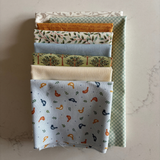 A stack of folded fabric pieces with various patterns and colours, including floral, checkered, and bird motifs, arranged on a light marble surface.
