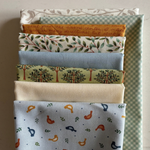 A stack of eight different patterned fabric squares in various colours and designs, including trees, birds, leaves, and stripes, arranged vertically on a neutral background.