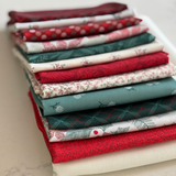 A stack of folded fat quarters in holiday-themed patterns, including red, green, white, and floral prints, arranged on a light surface.