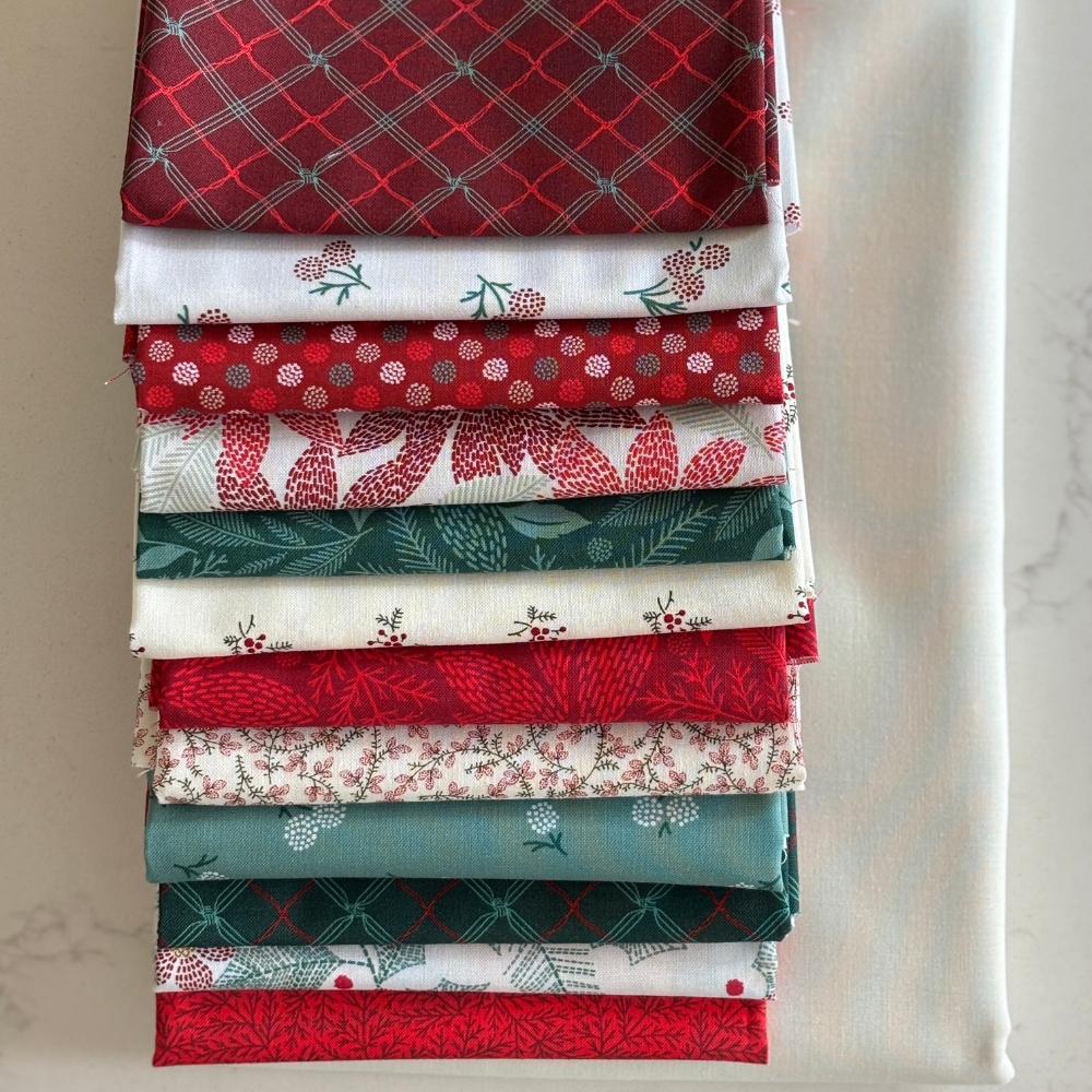 A stack of folded fat quarters with various holiday-themed patterns, including red plaid, white berry prints, and green foliage, arranged vertically on a light marble surface.