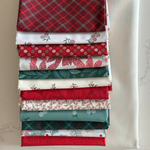 A stack of folded fat quarters with various holiday-themed patterns, including red plaid, white berry prints, and green foliage, arranged vertically on a light marble surface.