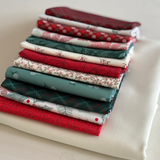 A stack of folded fat quarters pieces in holiday colours, including red, green, white, floral and geometric designs, arranged on a white fabric surface.