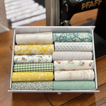 A white box filled with neatly fat quarters in assorted floral, gingham, striped, and patterned designs, placed on a wooden surface with a sewing machine in the background.