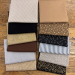 A stack of folded fat quarters with various patterns and colours, including gingham, floral, stripes, and metallic textures, arranged on a wooden surface.