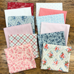 A collection of folded fat quarters with various patterns including florals, stripes, gingham, and plaid, arranged on a rustic wooden background.