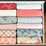 A collection of folded fat quarters in various patterns and colours, neatly arranged inside a white cardboard box.