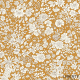 A repeating floral fabric pattern featuring white and cream flowers with green stems and leaves on a warm mustard yellow background. The brand name 'LIBERTY FABRICS' is printed in the bottom right corner.