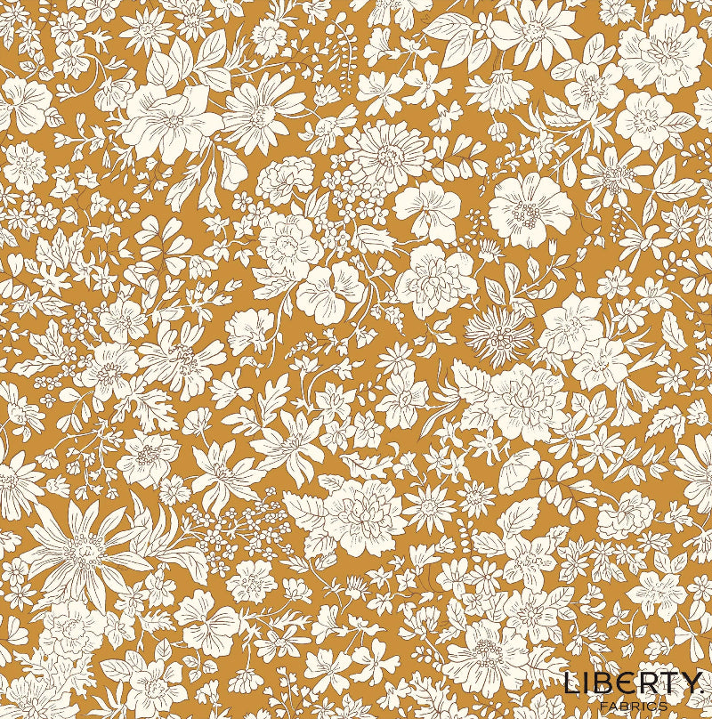 A repeating floral fabric pattern featuring white and cream flowers with green stems and leaves on a warm mustard yellow background. The brand name 'LIBERTY FABRICS' is printed in the bottom right corner.