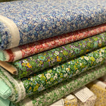 A stack of folded patterned Japanese lawn cotton fabric rolls in various colors and floral designs, including blue, red, green, and yellow prints, with some fabric tags visible.