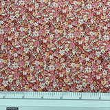 A close-up of a floral fabric pattern with small pink, white, and yellow flowers, shown with a metal ruler at the bottom for scale.