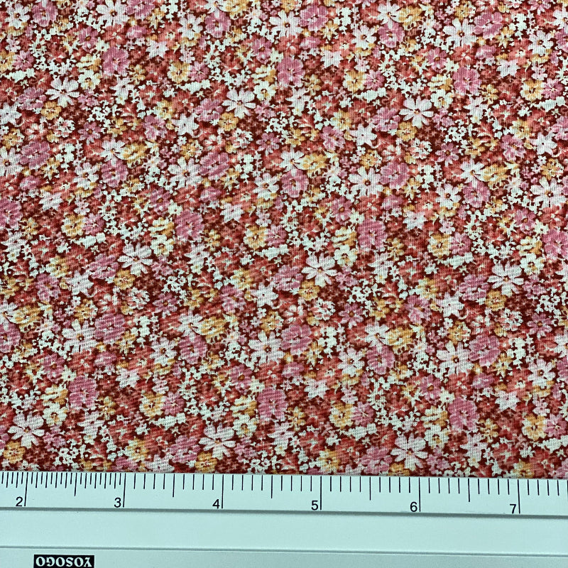 A close-up of a floral fabric pattern with small pink, white, and yellow flowers, shown with a metal ruler at the bottom for scale.