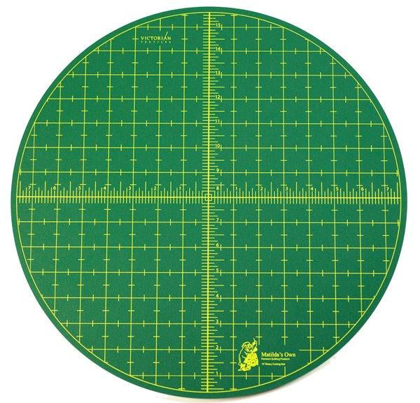 Round green cutting mat with grid lines and measurements on a white background